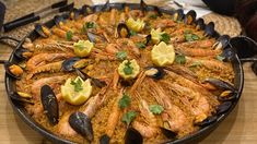 a large pan filled with seafood and clams on top of a wooden table next to utensils