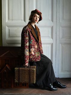 a woman sitting on top of a piece of luggage next to a dollhouse house