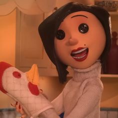 an animated doll holding a stuffed chicken in a kitchen with white cabinets and cupboards