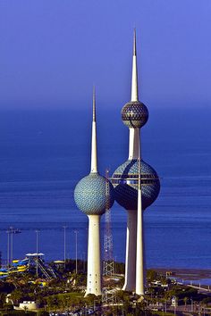 an aerial view of some very tall buildings by the ocean with blue water in the background