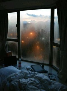 a bed sitting next to a window covered in rain