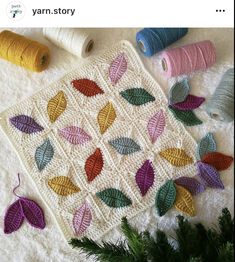 a crocheted blanket with leaves on it next to some yarn and thread spools