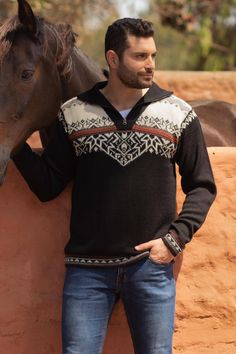 a man standing next to a brown horse in front of a red wall with his hands on his hips