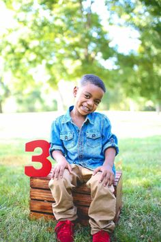 a young boy sitting on top of a wooden box with the number three in front of him