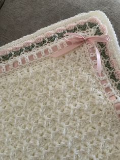 a crocheted blanket with pink ribbon on it