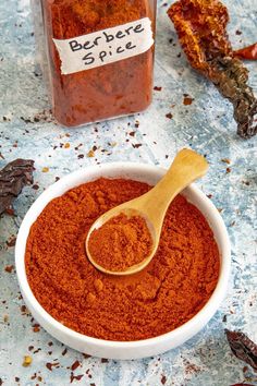 a wooden spoon in a white bowl filled with red chili powder next to a jar of pepper