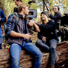 a group of people sitting on top of a log in the woods with cameras around them