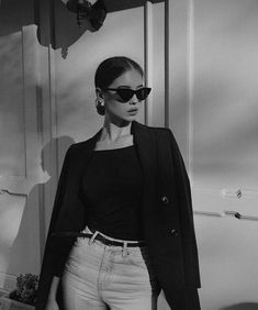 black and white photograph of a woman in sunglasses standing next to a wall with an open door