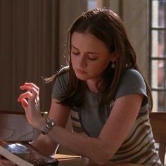 a woman sitting at a table with an open book in her hand and looking down