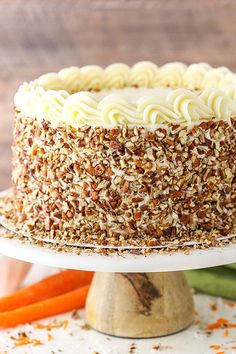 a carrot cake with white frosting and sprinkles on a plate next to sliced carrots