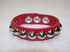 "1 Row Large 1/2\" Pyramid/Square Studs Genuine Leather Handcrafted Bracelet This a handcrafted, genuine leather 3/4\" wide Cuff/bracelet. The Leather is nice and soft, it will get buttery and more subtle with wear. The leather is available in vibrant colors. Racing Red Midnight Black Pretty Pink Arctic White Please check select color at time of check out. The studs/spikes are Standard US-77 1/2\" Cone studs. The cone studs measure 1/2\" in diameter. The studs are a conical shaped. The cone stud Adjustable Spiked Jewelry As Gift, Adjustable Spiked Jewelry For Gift, Adjustable Riveted Leather Bracelet Gift, Adjustable Leather Bracelet With Rivets, Adjustable Leather Bracelet With Rivets For Gift, Adjustable Spiked Leather Bracelets, Adjustable Red Wristband, Studs And Spikes, Wide Cuff Bracelets