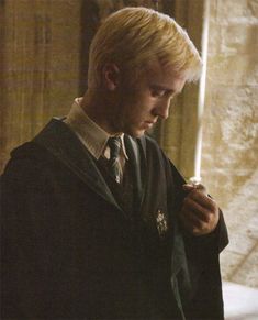 a man with blonde hair wearing a harry potter robe and holding a wand in his hand