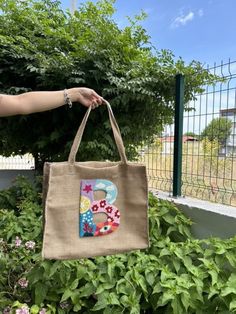 a person holding a bag with the letter b on it in front of some bushes