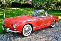 an old red car is parked on the gravel in front of some trees and grass