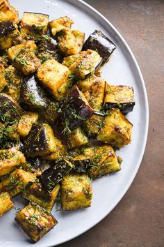 a white plate topped with cooked eggplant and herbs