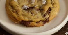 a chocolate chip cookie on a plate with sea salt and coconut flakes around it