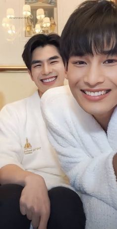 two young men sitting next to each other with towels on their shoulders and one holding a cell phone