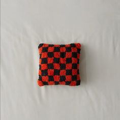 an orange and black checkered pillow on a white surface