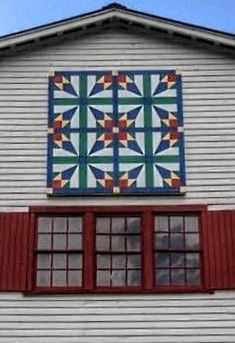 a white building with red shutters and a quilt on the window sill above it