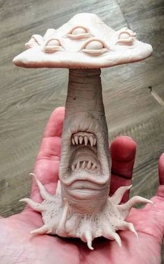 a hand holding a clay sculpture of a mushroom with its mouth open and teeth out