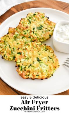 two zucchini fritters on a white plate next to a small bowl of yogurt