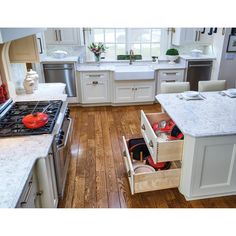 an open drawer in the middle of a kitchen with wooden floors and white cabinets,