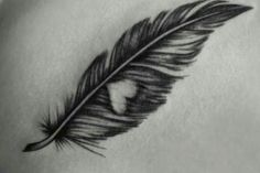 a black and white photo of a feather on the back of a woman's shoulder