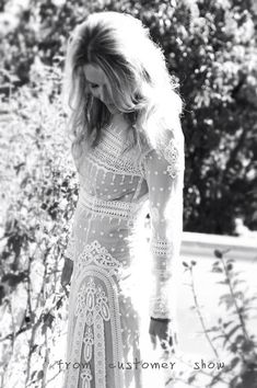 black and white photograph of a woman in a long dress standing next to some bushes