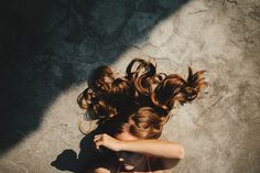 a woman laying on the ground with her hair flying in the air and looking down