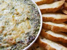 there is a white bowl filled with bread and spinach dip on the plate next to it