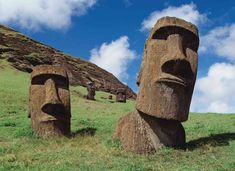 two large carved faces on the side of a hill with grass and blue sky in the background