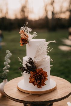 a three tiered white wedding cake decorated with flowers and feathers sits on a wooden table