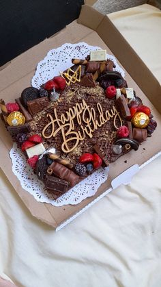 a birthday cake in a box with the words happy birthday written on it, surrounded by assorted candies and chocolates