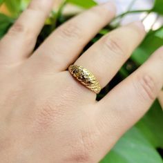 a woman's hand with a gold ring on it and green leaves in the background