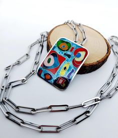 Make a statement with this bold geometric cloisonné enamel pendant! The rectangular pendant is meticulously handcrafted from fine silver, featuring an abstract design in vibrant colors like red, green, blue, and yellow. The intricate cloisonné enamel work adds an artistic flair, perfect for those who love unique, standout jewelry pieces. This eye-catching pendant is paired with a modern stainless steel chain with chunky links, creating a striking contrast between the contemporary chain and the c Cloisonne Enamel Jewelry, Colorful Artwork, Cloisonne Enamel, Necklace Unique, Unique Handmade Jewelry, Enamel Jewelry, Unique Necklaces, Steel Chain, Stainless Steel Chain