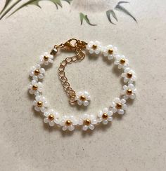 a bracelet with white beads and gold accents on a marble counter top next to flowers