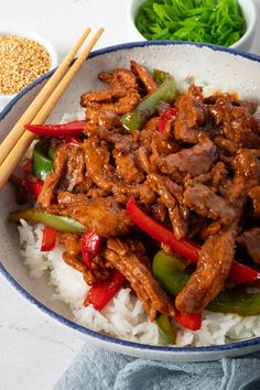 a bowl filled with meat and vegetables on top of rice next to chopsticks