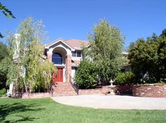 a brick house with trees and bushes around it's front entrance, on a sunny day