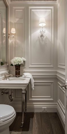 a white toilet sitting next to a sink under a bathroom mirror with lights on it