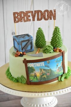 a fortnite themed birthday cake is displayed on a pedestal with trees and a sign