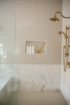 a bathroom with marble tile and gold fixtures, including a shower head in the corner