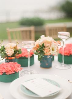 the table is set with wine glasses and flowers in vases on top of each other