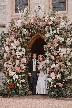 a bride and groom standing in front of a floral arch