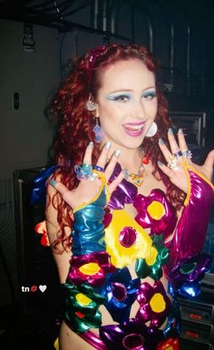 a woman with red hair is dressed in colorful clothing and has rings on her fingers