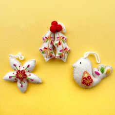 three embroidered ornaments are sitting on a yellow surface, one is red and the other is white