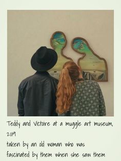 two people standing next to each other looking at artwork