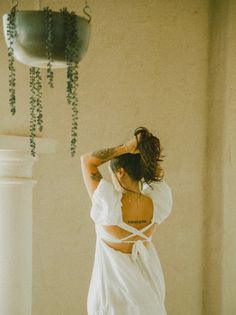 a woman standing in front of a mirror wearing a white dress and holding her hair back