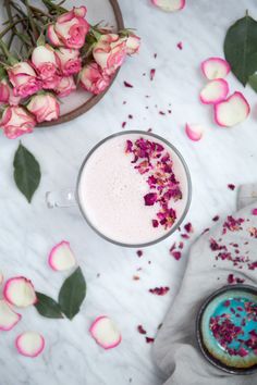 a glass cup filled with pink flowers next to a plate full of roses and petals