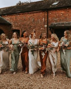 a group of women standing next to each other in front of a brick building holding bouquets