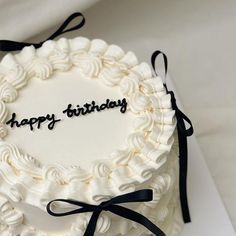 a happy birthday cake with white frosting and black ribbon around it on a table